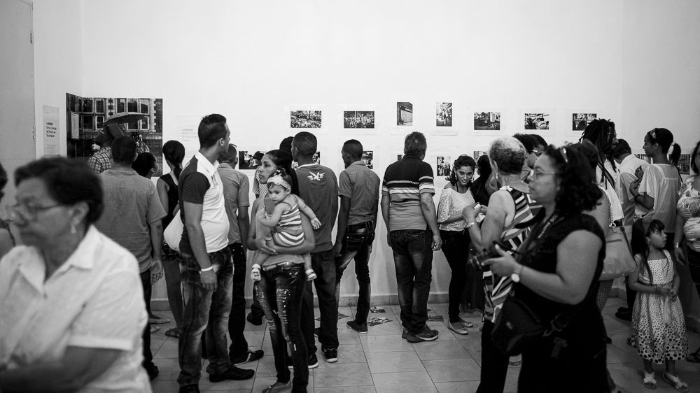 Image of gallery attendants at "Londres. Detrás y debajo del Palacio de Buckingam" exhibition space. Arte Soy Gallery in Santiago de Cuba, Cuba.. This is an image related to a project inside Pedro Rodrigues (Treze413) graphic design portfolio.